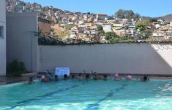 Treze crianças em piscina praticando natação; ao fundo, aglomerado da Serra.